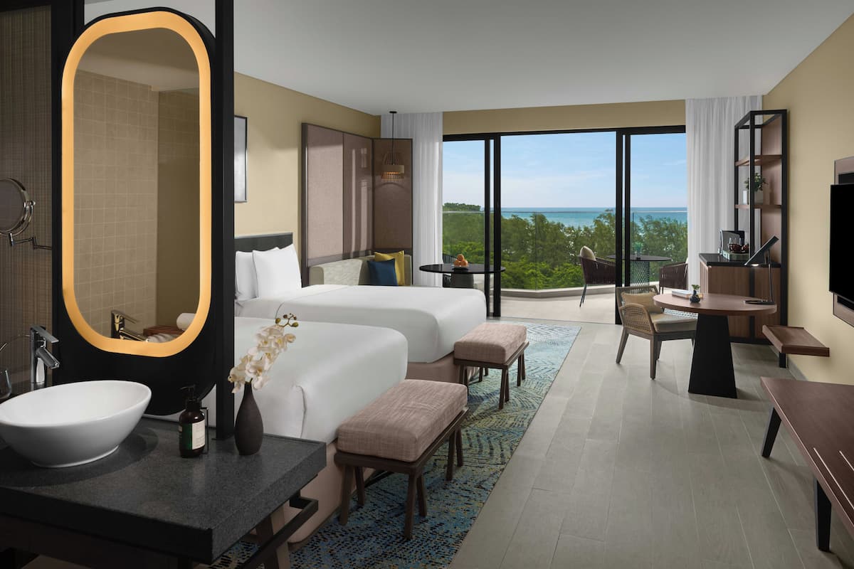 Een hotelkamer met twee bedden, een grote spiegel, een badkamer met wastafel en een balkon met uitzicht.