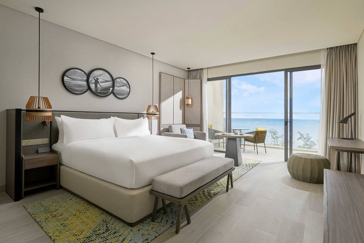 Een moderne hotelkamer met een groot bed, een klein bureau, een stoel en uitzicht op de oceaan.