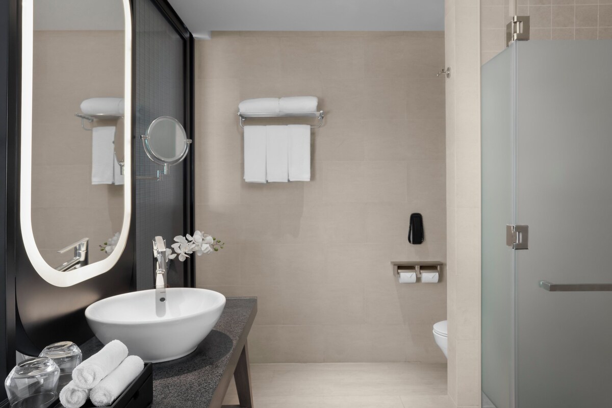 Een moderne badkamer met een groot ovaal wastafel, een ronde spiegel, een douchecabine van glas en een toilet.