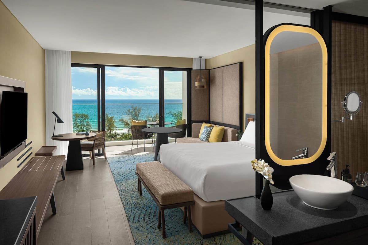 Een hotelkamer met een groot bed, een bureau, een televisie, een badkamer met een grote spiegel en uitzicht op de oceaan.