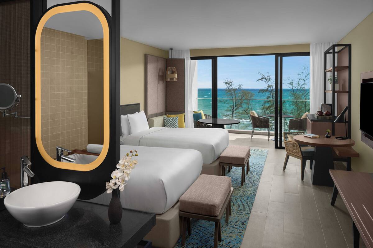 Een hotelkamer met een grote spiegel, een bed, een bureau, een stoel, een klein tafeltje, een televisie en uitzicht op de oceaan.