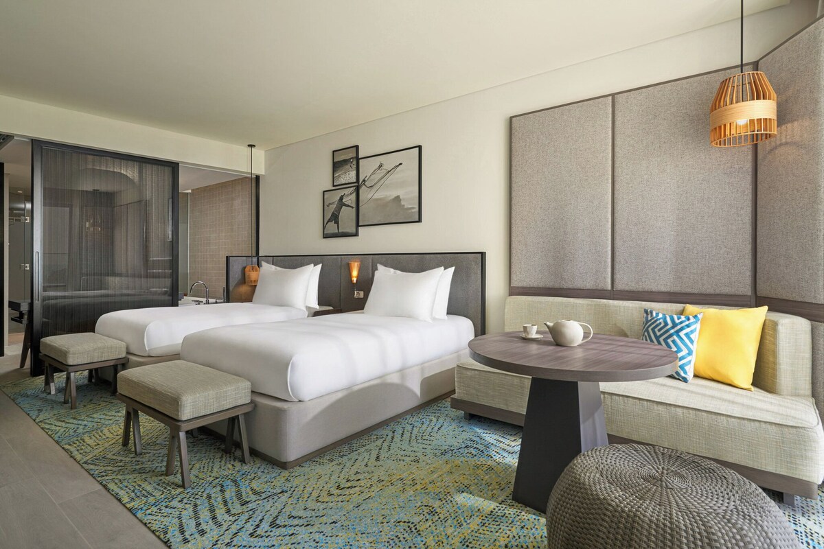 Een moderne hotelkamer met twee bedden, een bank, een ronde tafel en een groot raam.