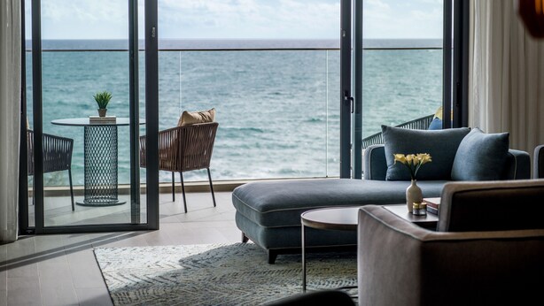Een moderne woonkamer met een grote glazen schuindeur die leidt naar een balkon met uitzicht op zee.