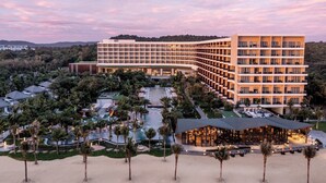 Een hotel met een modern design, bestaande uit een gebogen gevel, meerdere verdiepingen en een centrale binnenplaats met palmbomen en een zwembad.