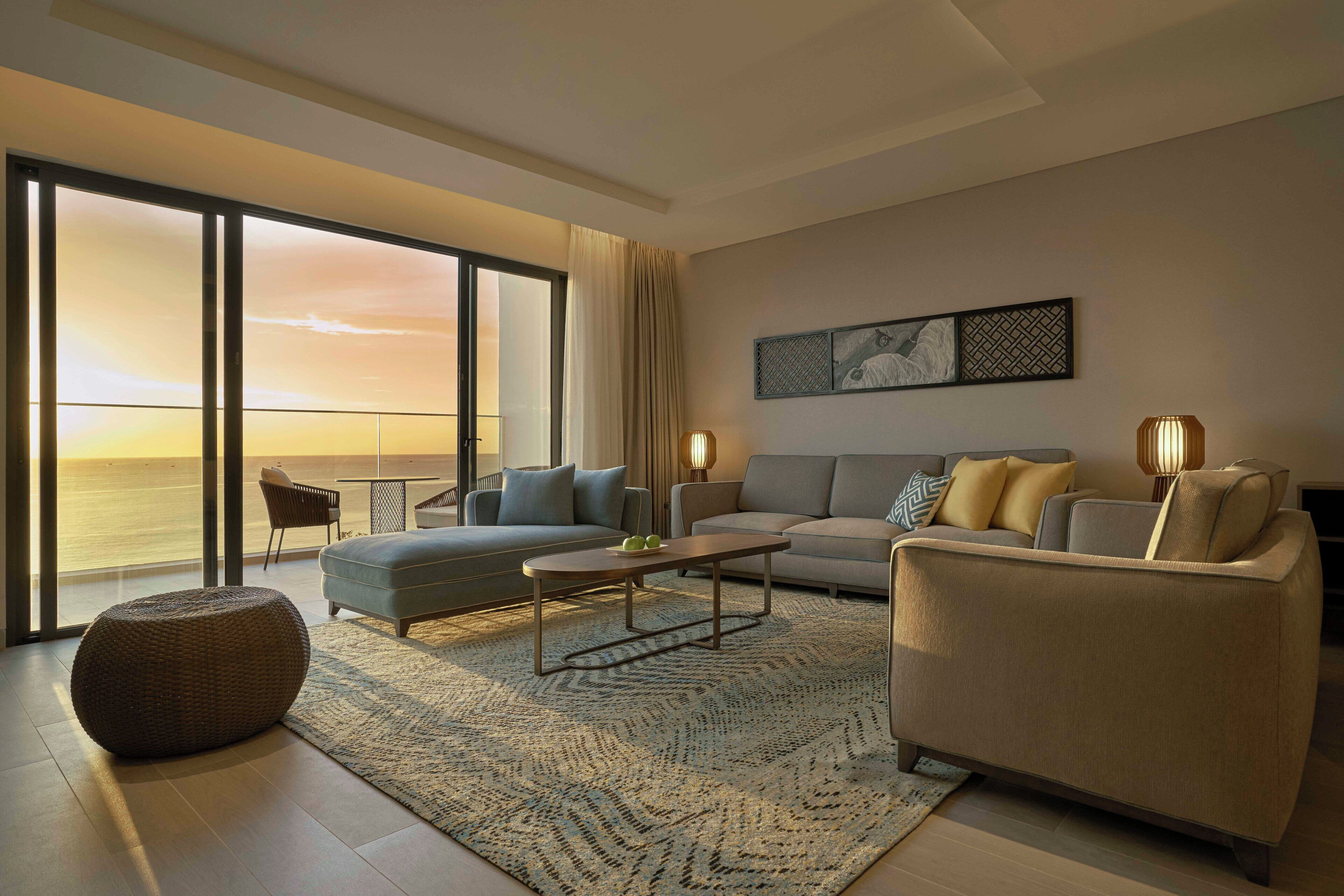 A modern living room with a large window overlooking the ocean, a sofa, a coffee table, and a patterned rug.