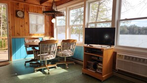 A cozy cabin interior with a wooden dining table, two chairs, a television, and a bookshelf. - Weekly discounts avail. Get away from it all on the start of  The Belgrade Lakes (Oakland)