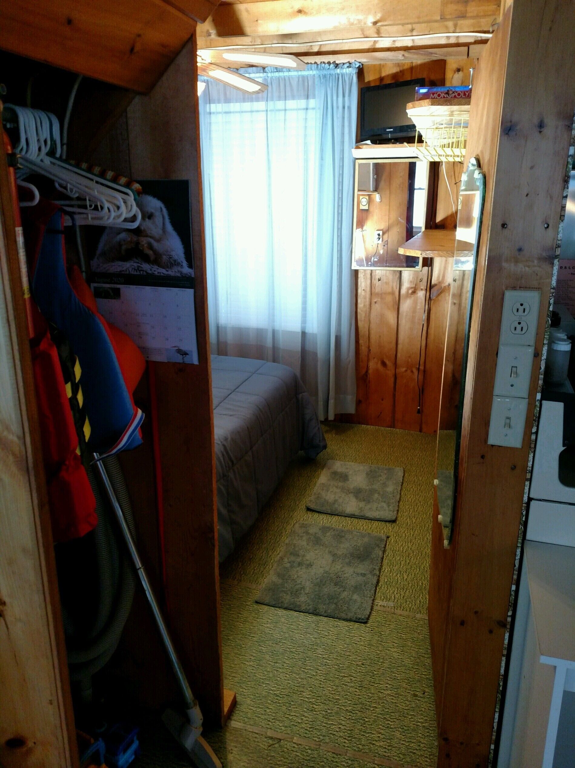 Un interior pequeño y de madera con una cama, un escritorio pequeño y un perchero.