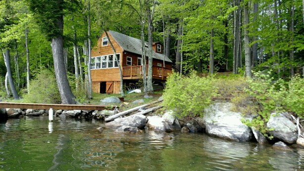 A wooden cabin with a deck, surrounded by trees and a body of water. - Weekly discounts avail. Get away from it all on the start of  The Belgrade Lakes (Oakland)