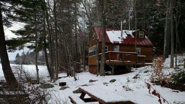 Une cabane avec une façade en bois, une terrasse et une table de pique-nique recouverte de neige.