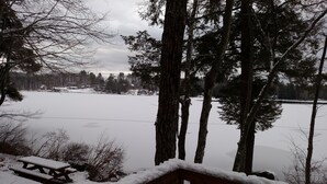 A wooden deck with a snow-covered picnic table and benches, overlooking a frozen lake with trees and houses in the background. - Weekly discounts avail. Get away from it all on the start of  The Belgrade Lakes (Oakland)