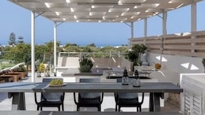 Une terrasse extérieure couverte, dotée d’une table et de chaises, offrant une vue panoramique sur la mer.