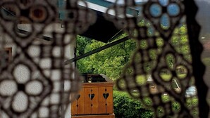 Vista a través de una reja decorativa de un patio con un armario de madera, una mesa y sillas.