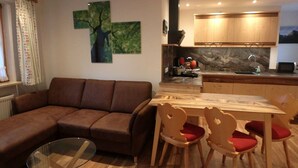 Una sala de estar moderna con un sofá marrón, una mesa de centro de vidrio y una mesa de comedor de madera con cuatro sillas.