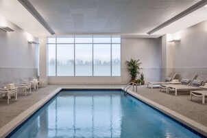 Piscina con sillones de descanso y un ventanal grande.