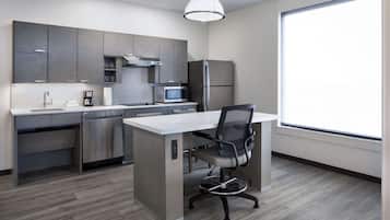 A modern kitchen with grey cabinets, stainless steel appliances, a white countertop, and a black office chair.