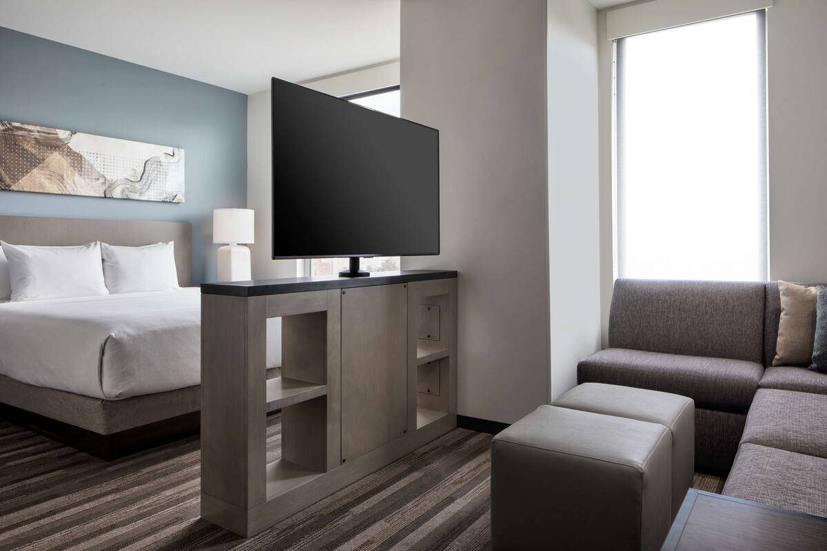 A hotel room with a bed, a TV on a stand, a sofa, and a window.