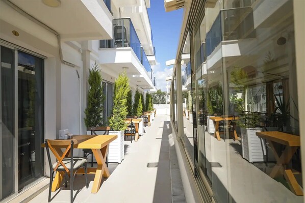 Un espacio al aire libre moderno con mesas y sillas, rodeado por paredes de vidrio y plantas en macetas.