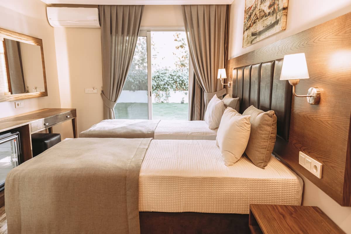 A hotel room with two beds, a desk, a mirror, and a window with curtains.