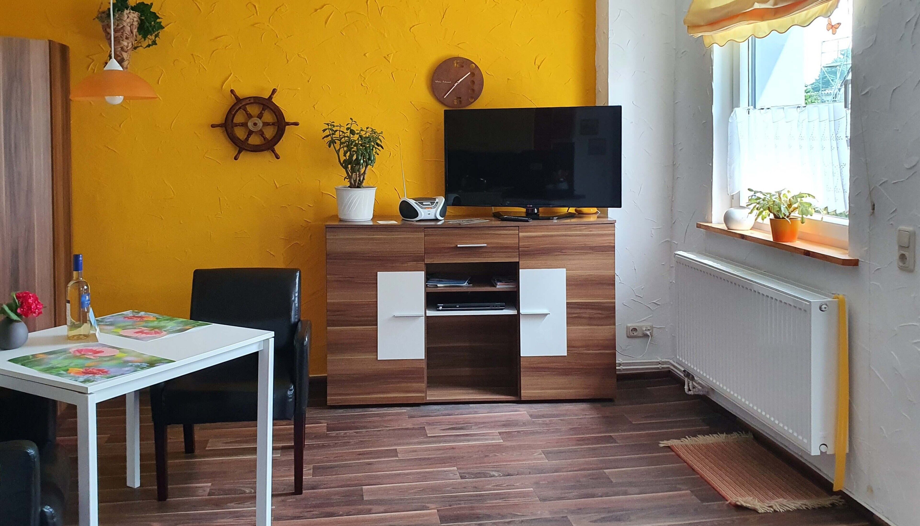 A compact living space with a wooden cabinet, a television, a clock, a potted plant, and a window with a view.