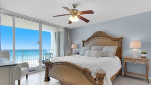 A spacious bedroom with a large bed, a ceiling fan, a nightstand, and a view of the ocean.