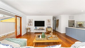 A modern living room with a flat-screen TV, wooden flooring, and a dining area with wicker baskets. - Sea Deck, Hyams Beach, Jervis Bay (Hyams Beach)