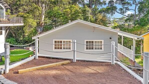 A small, single-story building with a white exterior, a covered porch, and a fenced area. - Sea Deck, Hyams Beach, Jervis Bay (Hyams Beach)