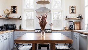 Een moderne keuken met een houten tafel, twee stoelen, een vaas met gedroogde planten, een magnetron, een fornuis en een vaatwasser.