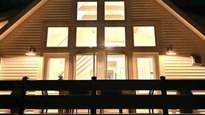 Een houten blokhut met een puntig dak en meerdere ramen, verlicht door binnenverlichting.