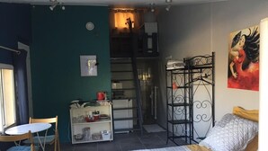 Une chambre à coucher avec un lit, un bureau, une chaise, une étagère contenant des ustensiles de cuisine, une échelle et un tableau accroché au mur.