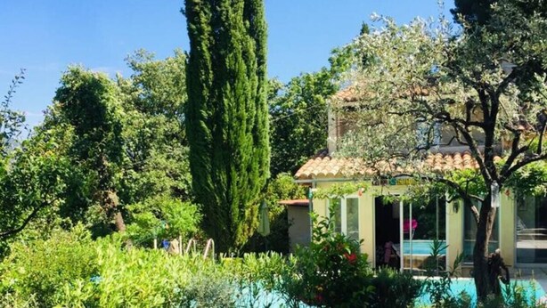 Un jardin avec une piscine, de grands arbres et un bâtiment doté d’un toit en tuiles.