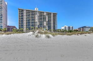 Un hôtel situé en bord de mer, avec plusieurs étages, une tour centrale imposante et une plage de sable.