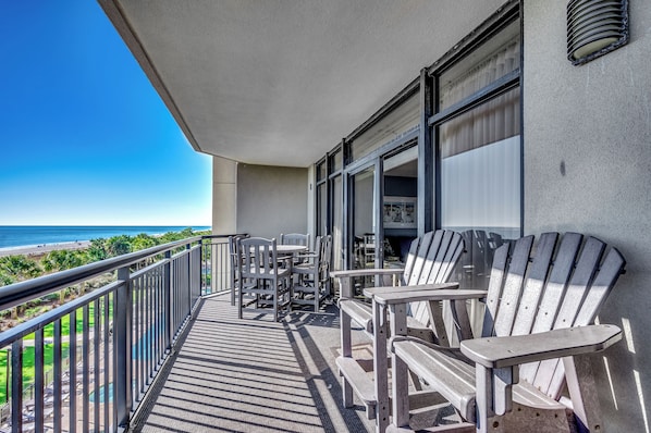 Un balcon avec des fauteuils Adirondack, une table et une vue sur la plage.