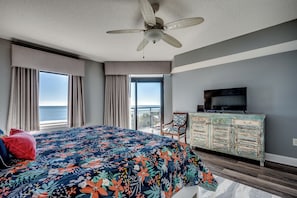 Une chambre dotée d’un grand lit, d’un ventilateur de plafond, d’une télévision, d’une commode et d’un balcon offrant une vue sur l’océan.