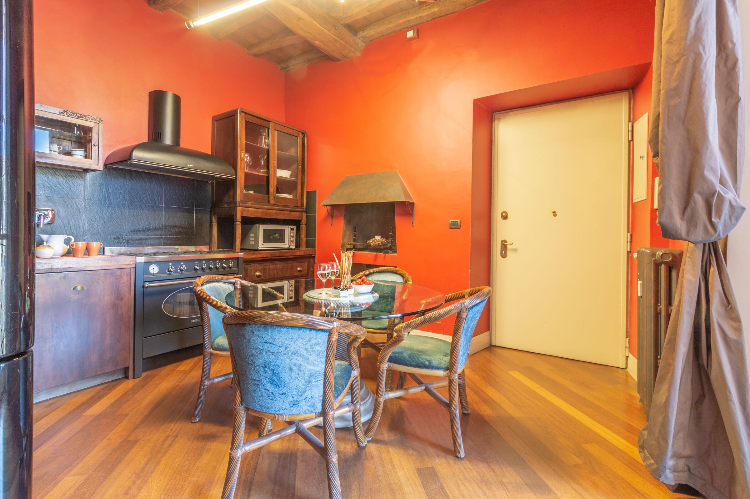 A kitchen with a red wall, wooden cabinets, a stove, and wicker chairs.