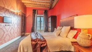 Quarto de hotel com cama, mesa de cabeceira com abajur, televisão e janela com cortinas.