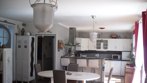 A modern kitchen with white cabinets, a dining area with a round table and chairs, and a living room with a sofa. - Gites de Daumesnil 5 minutes walk from town center. (Morlaix)