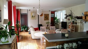 A cozy living room with a fireplace, a dining area with a round table, and a kitchen with wooden cabinets and a bar counter. - Gites de Daumesnil 5 minutes walk from town center. (Morlaix)