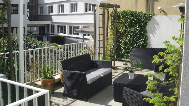 An outdoor balcony with wicker furniture, potted plants, and a white pergola. - Gites de Daumesnil 5 minutes walk from town center. (Morlaix)