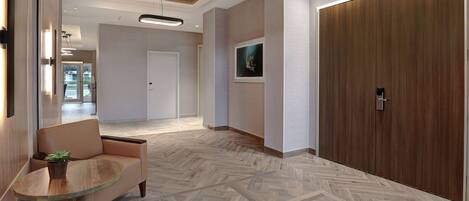 A modern lobby with a herringbone-patterned floor, a seating area with a glass table, and a large wooden door.