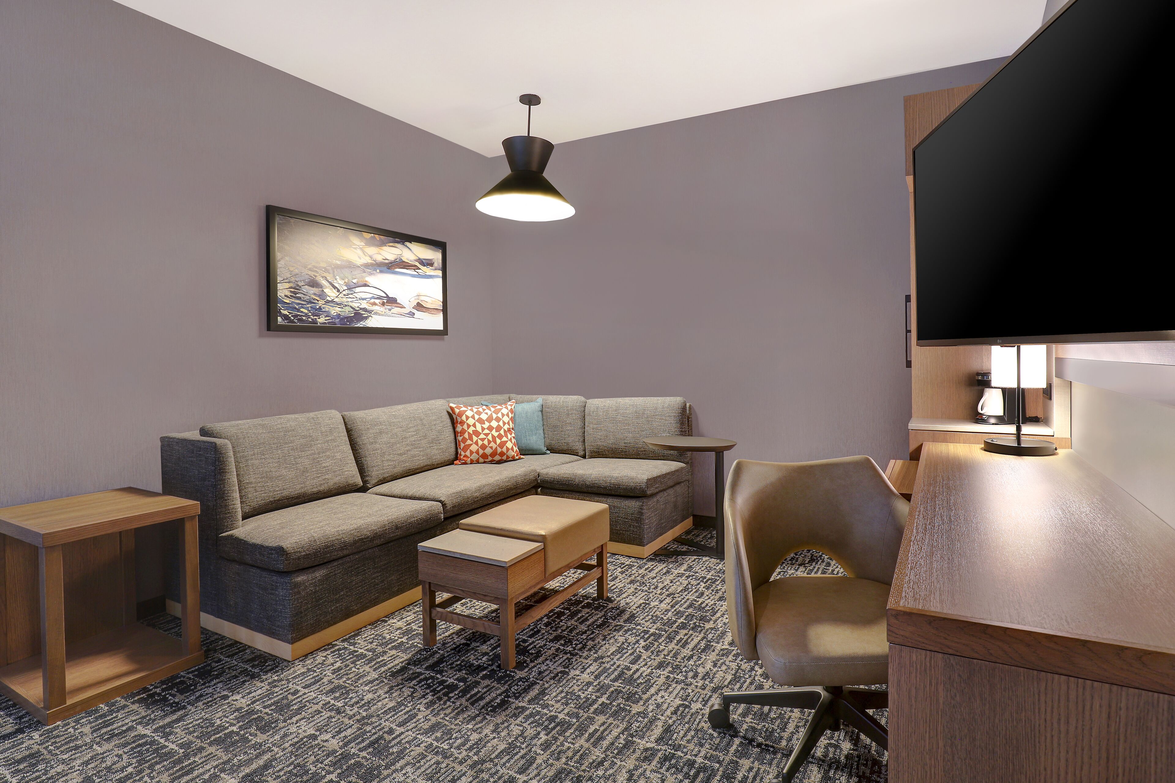 A modern living room with a sectional sofa, a wooden coffee table, a side table, a television, and a lamp.