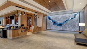 Un moderno vestíbulo de hotel con un mostrador de recepción de madera, una gran obra de arte abstracta en la pared y un área de descanso con una lámpara.