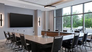 A conference room with a long table, chairs, a flat-screen TV, and large windows offering a view of the outdoors.