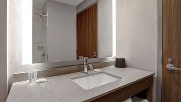 A modern bathroom with a large mirror, two sinks, a shower, and a wooden door.