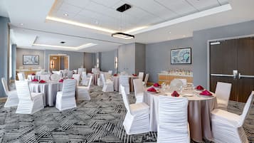 Un amplio salón de banquetes con varias mesas redondas, cada una con sillas blancas y servilletas rojas.