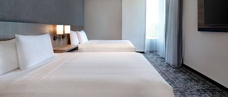 Une chambre d’hôtel avec deux lits, un téléviseur à écran plat, une table de chevet avec une lampe et une grande fenêtre avec des rideaux.