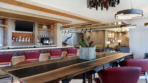 Un bar moderno con una mesa de madera larga, sillas rojas y una variedad de botellas de licor.