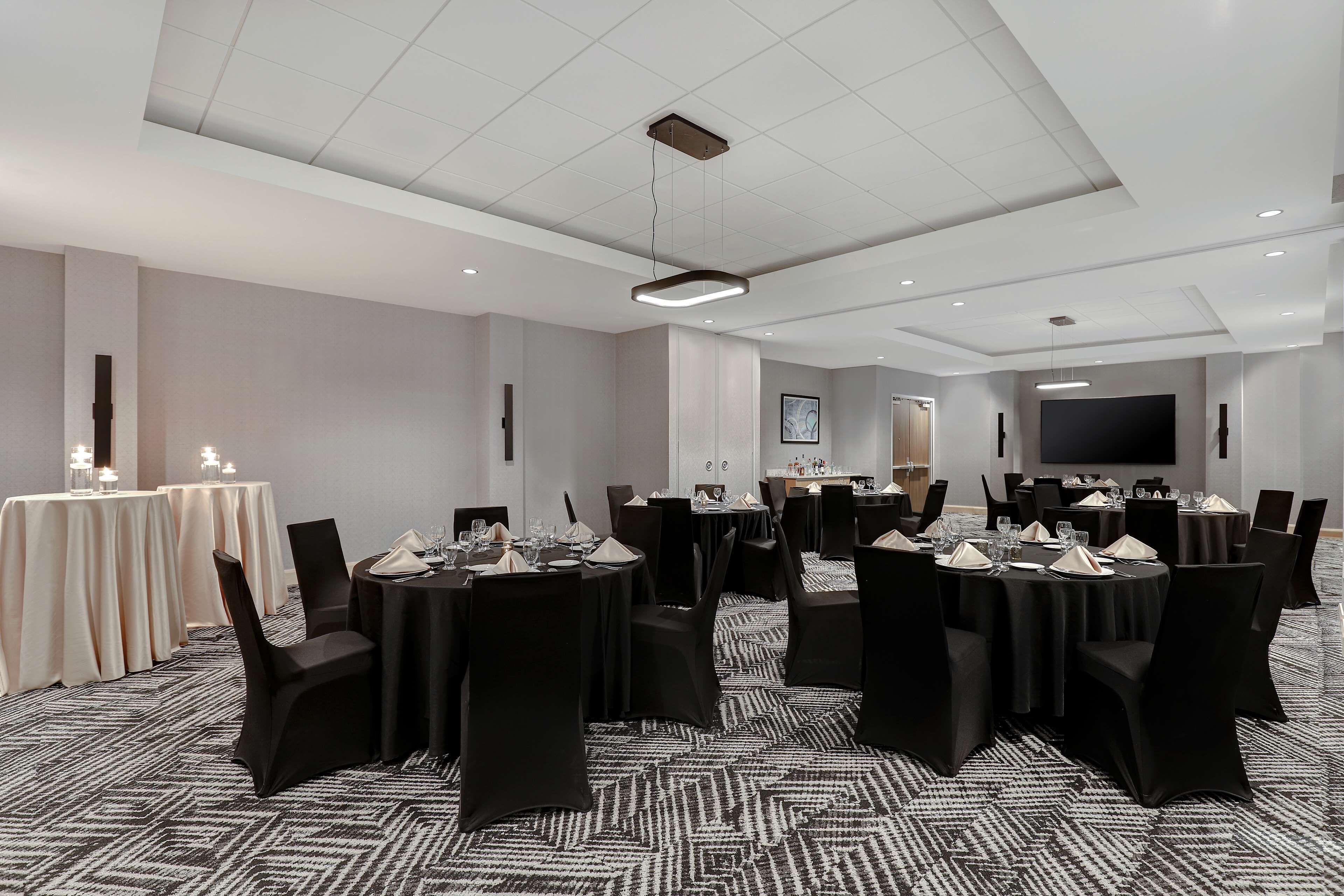 A conference room with multiple tables, black chairs, and a large screen.