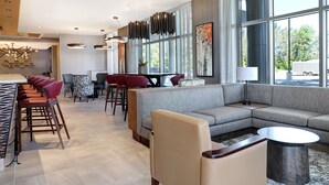 Un moderno vestíbulo de hotel con zona de bar, asientos y grandes ventanales con vistas al exterior.