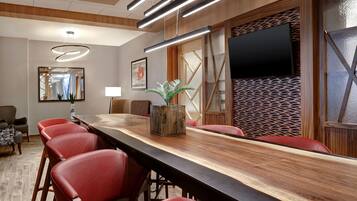 Un salón de conferencias con una larga mesa de madera, sillas rojas, una planta en maceta, un televisor de pantalla plana y modernas luminarias.