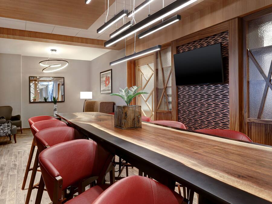 A conference room with a long wooden table, red chairs, a potted plant, a flat-screen TV, and modern lighting fixtures.